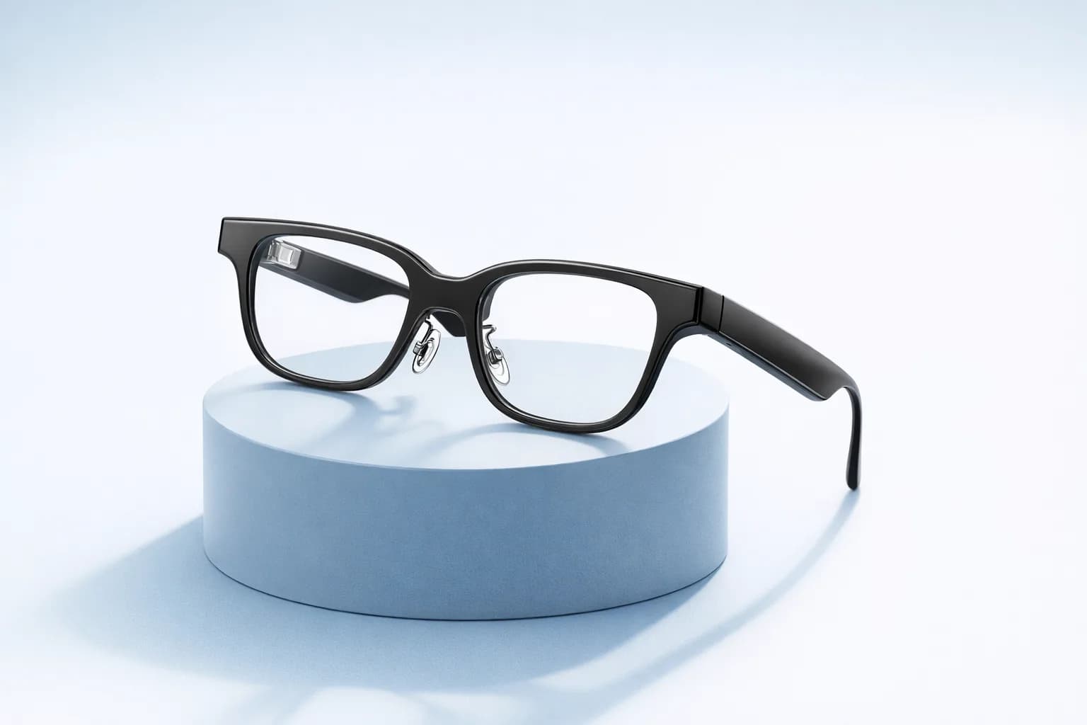 Gafas inteligentes AirCaps en negro, en ángulo sobre un pedestal azul claro, con la montura cuadrada gruesa y un módulo en la patilla.