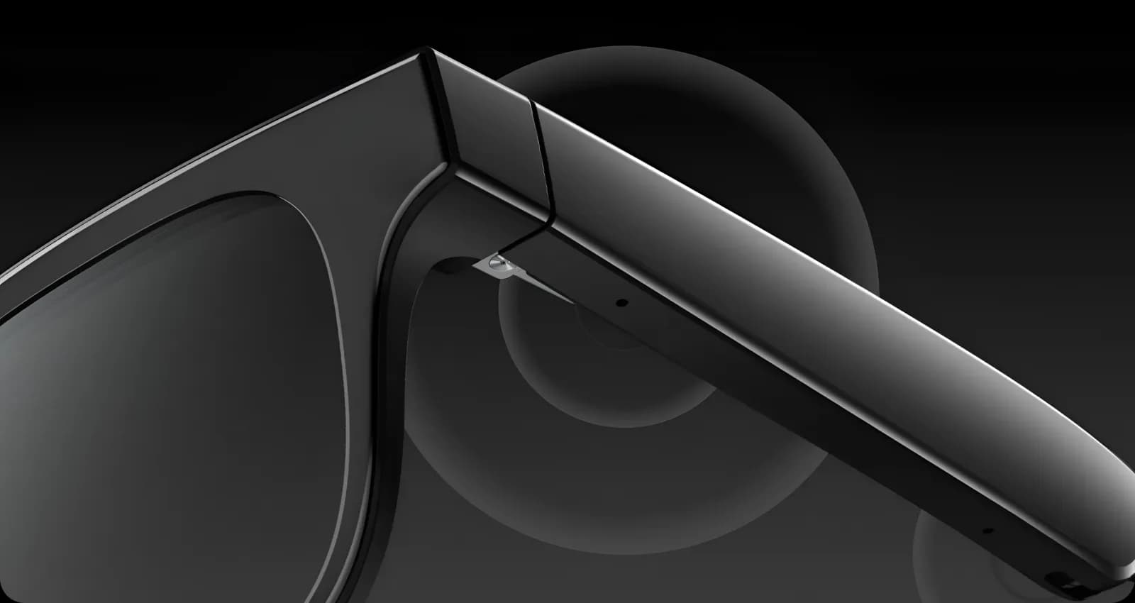 Gafas inteligentes AirCaps en negro, primer plano de la bisagra de la patilla, con una pequeña abertura de micrófono sobre fondo oscuro.