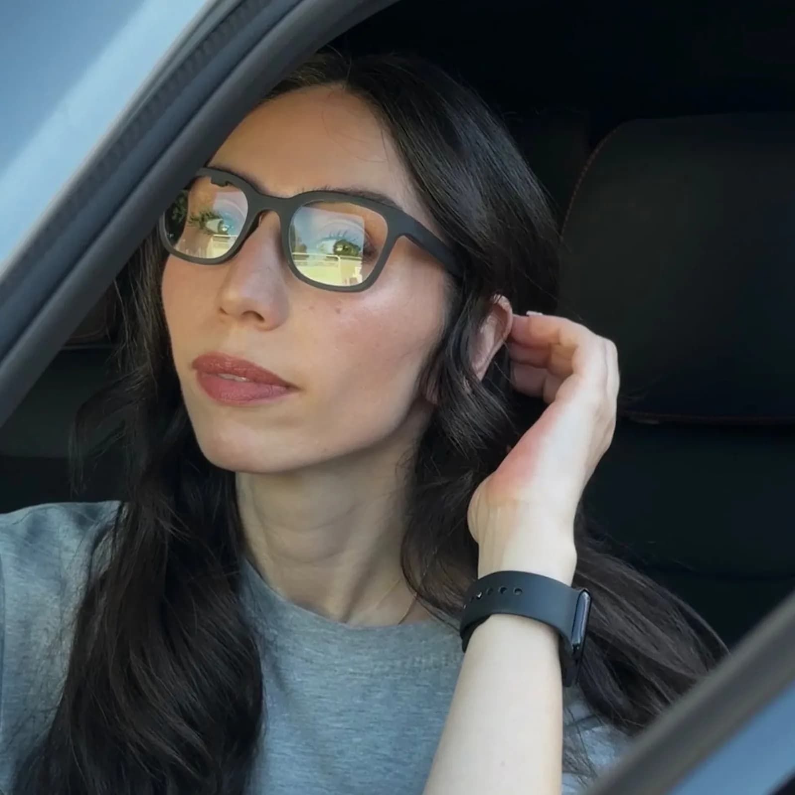 Gafas Brilliant Labs Halo en negro en el rostro de una mujer dentro de un auto, con la lente reflejando un tono amarillento de luz solar.