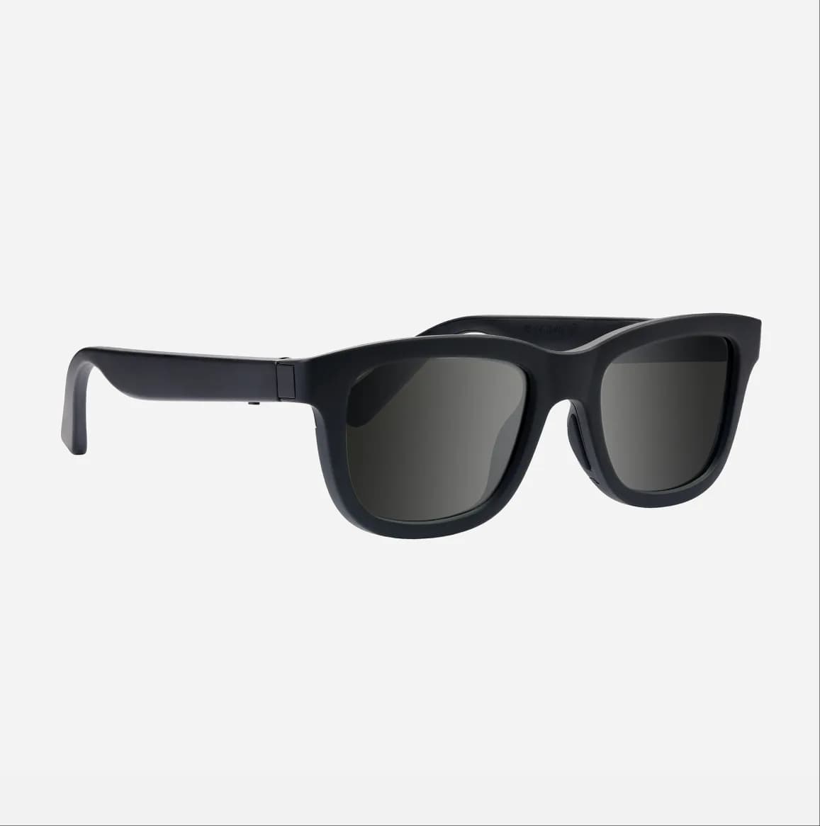 Gafas de sol inteligentes Chamelo Dusk en negro, montura cuadrada gruesa, en tres cuartos sobre fondo gris claro liso.
