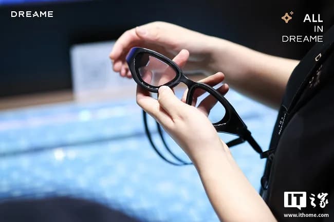 Dreame AQUA 100 swim glasses held in a hand at a trade show, showing the black frame's side and a thin cable running to the ear speaker.