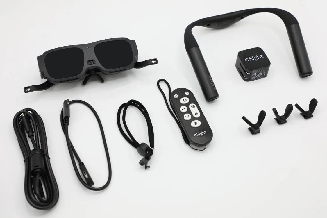eSight Go黑色护目镜平放，旁边是遥控器、充电线和头戴式衬垫。