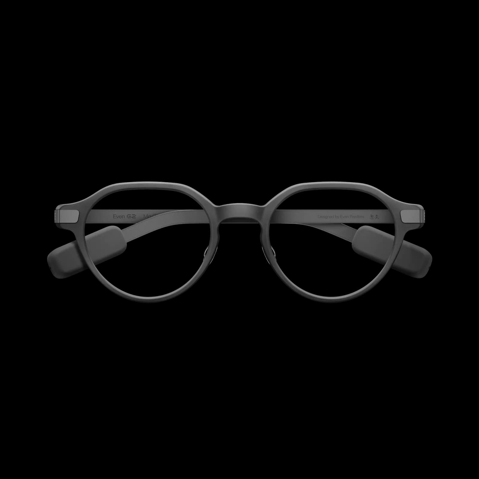 Gafas inteligentes Even Realities G2 en gris oscuro, montura redonda con cápsulas de carga gruesas en ambas patillas, sobre fondo negro.