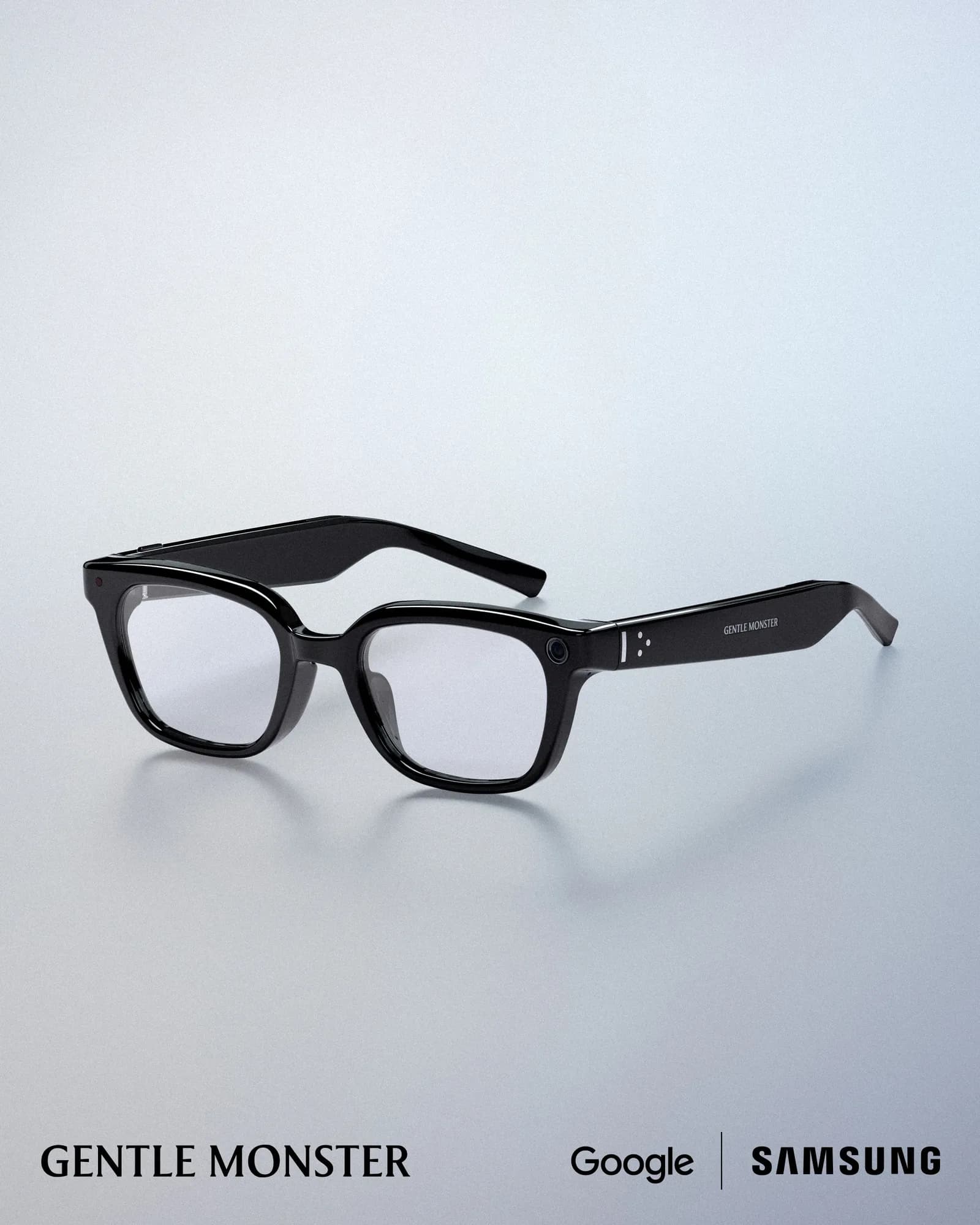 Gafas Gentle Monster Intelligent Eyewear en negro brillante, montura cuadrada con cristales transparentes y cámara pequeña en el aro izquierdo, fondo claro.