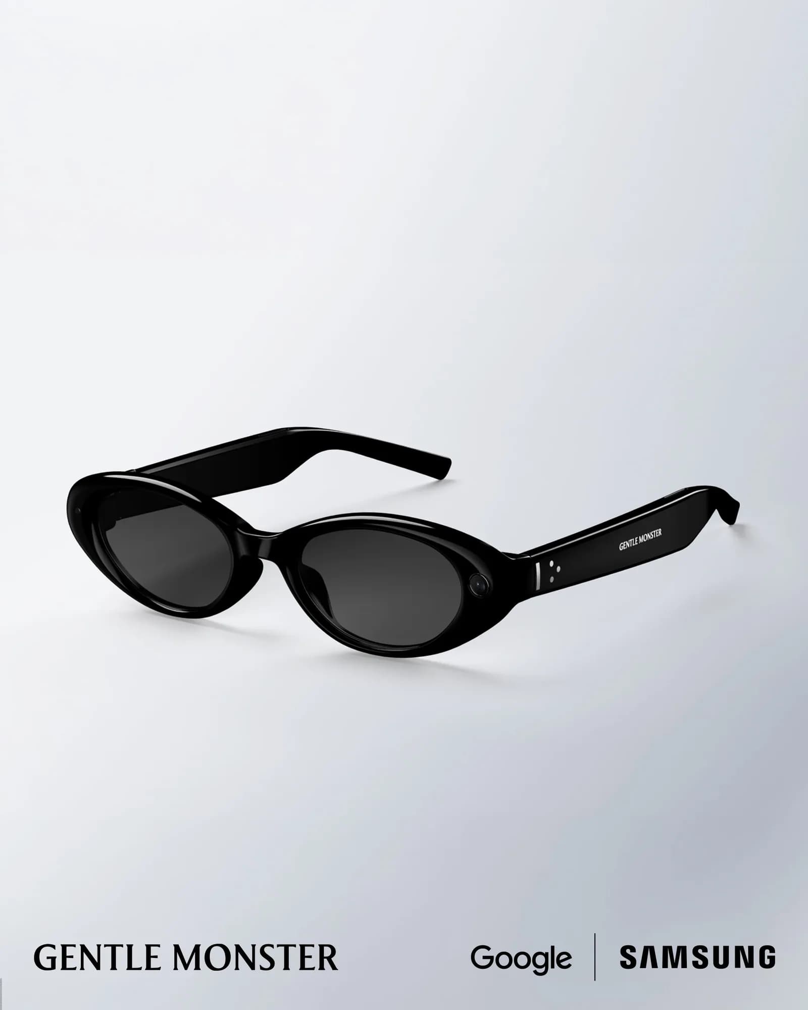 Gafas Gentle Monster Intelligent Eyewear en negro brillante, montura ovalada con cristales oscuros y cámara pequeña en el aro izquierdo, fondo claro.
