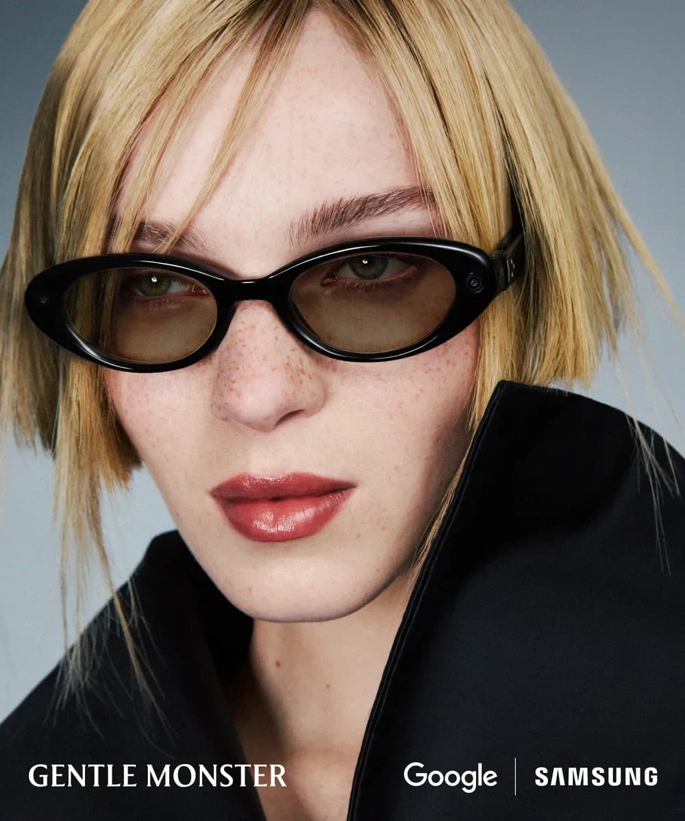 Gafas Google Android XR Audio Glasses en negro, montura ovalada con cristales oscuros, puestas de cerca por una mujer con abrigo negro de cuello alto.