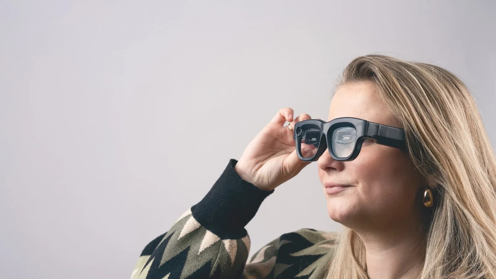 Gafas Luna Glass sostenidas cerca del rostro de una mujer, en negro, mostrando de cerca la cámara y el patrón de líneas en el lente.