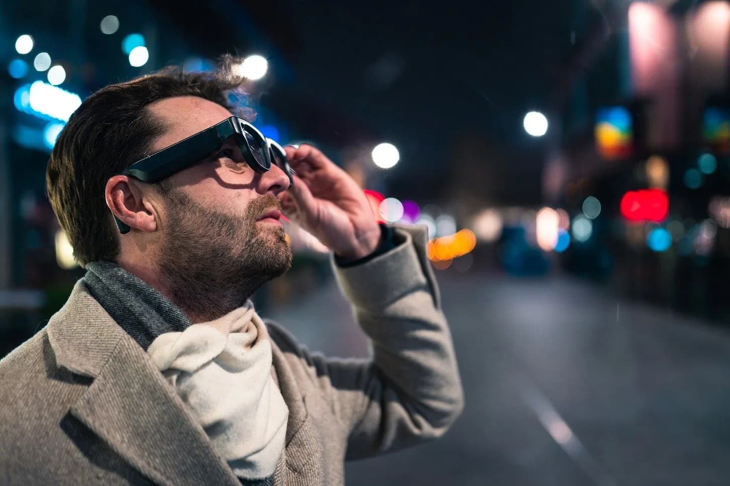 Gafas Luna Glass usadas al aire libre por la noche por un hombre que ajusta los lentes oscurecidos, con luces de la ciudad desenfocadas detrás.