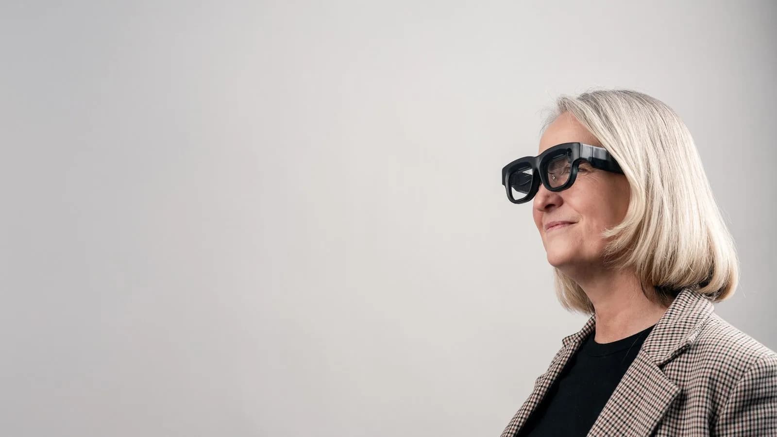 Gafas Luna Glass usadas de perfil por una mujer, con la montura negra gruesa y la patilla visibles sobre un fondo gris liso.