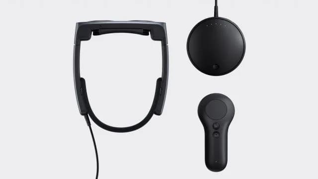 Magic Leap 2, visor oscuro, disco de cómputo redondo y mando de mano dispuestos sobre un fondo gris.