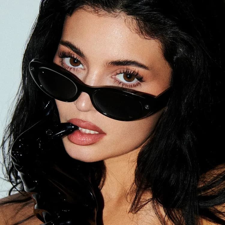 Meta Glasses Starfire worn by a woman, close-up on her face showing the black oval frame and a camera lens on the temple.