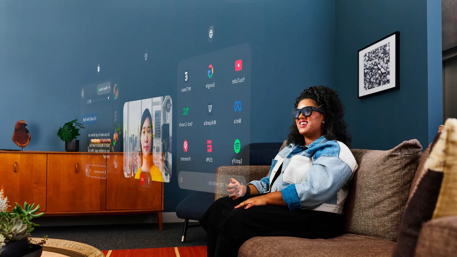 Meta Orion prototype glasses worn by a woman on a couch, black rectangular frame with translucent floating app panels beside her.
