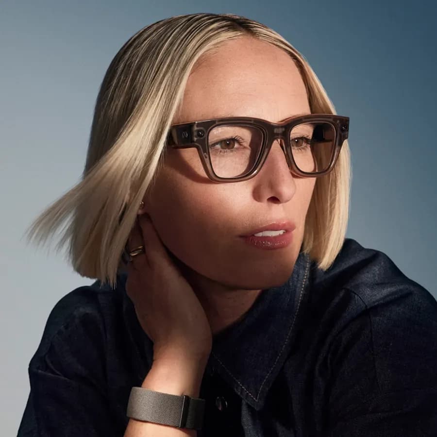 Gafas Meta Ray-Ban Display en marrón translúcido, montura cuadrada usada por una mujer con la Meta Neural Band visible en la muñeca cerca del rostro.