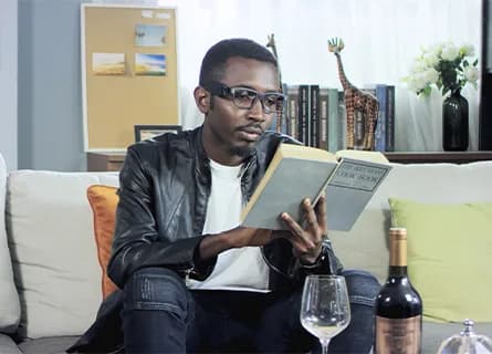 NextVPU AngelEye Smart Reader clipped to rectangular glasses worn by a man reading a book on a couch.