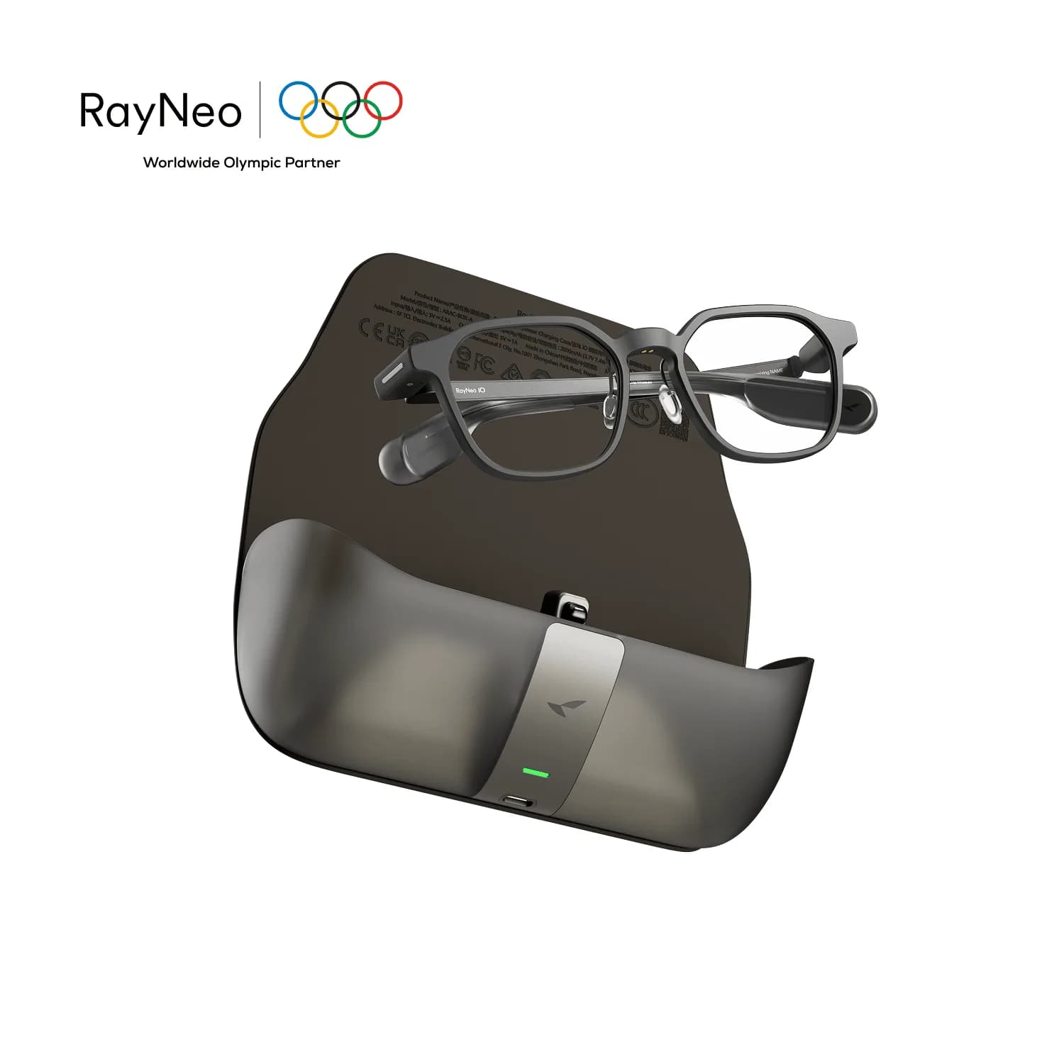 Gafas RayNeo iO en negro, apoyadas sobre su estuche de carga, con el puerto USB-C y la luz verde visibles.