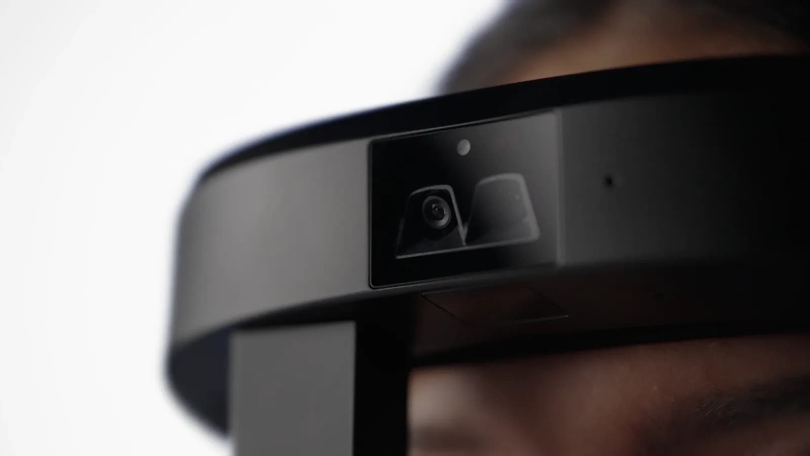 RealWear Arc 3 headset in black, close up on the front camera module and sensor on the headband, worn on a blurred head.