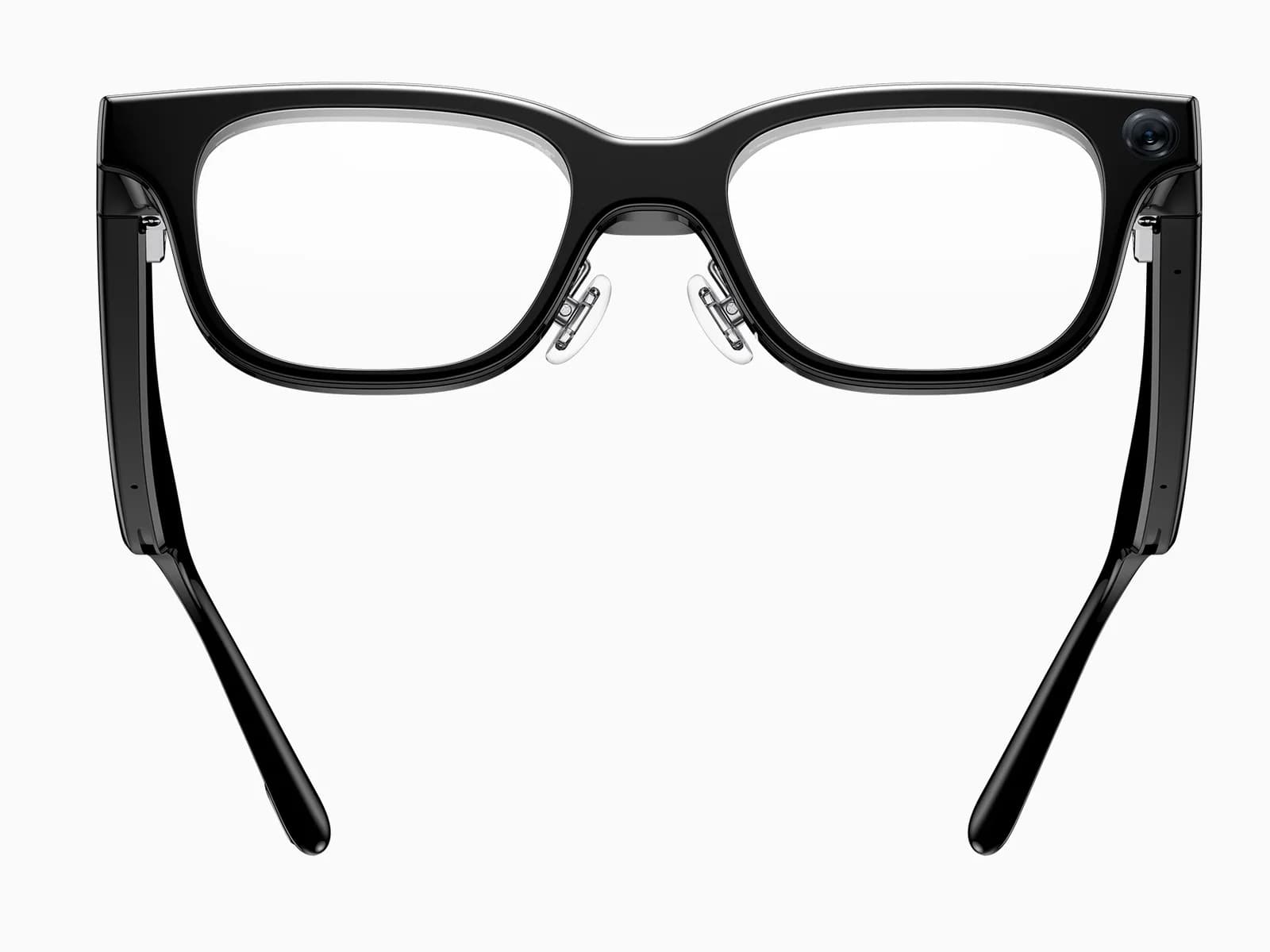 The Rokid Glasses RV101 seen from above and behind, temples splayed as if resting on a table: the camera shows on the outer corner of the right rim, the hinges and the metal contacts of the charging cable are visible, and the temples taper to a rounded tip.