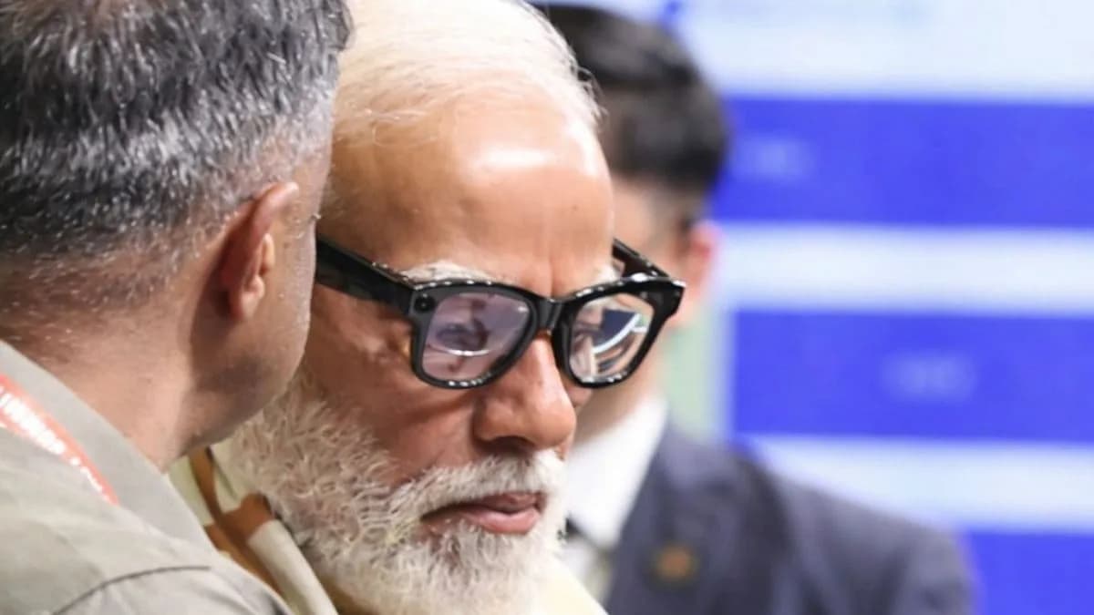 Sarvam Kaze in thick black rectangular frames, worn by a bearded man photographed from the side, with people blurred behind him.
