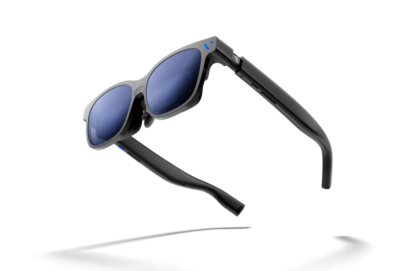The Viture Beast alone on a white background, seen from above at an angle with the temples open: a squared frame in black and grey with wide dark blue lenses, thick temples that curve down at the tip, and a soft shadow underneath.