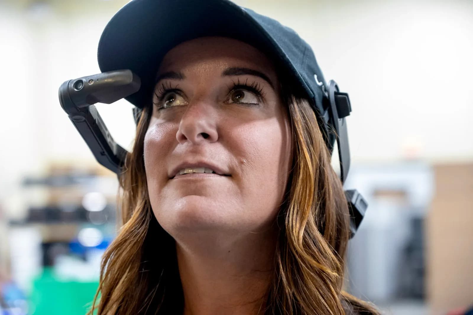 Una mujer usa el módulo del Vuzix LX1 sujeto a la visera de la gorra, mirando hacia arriba en un almacén desenfocado al fondo.