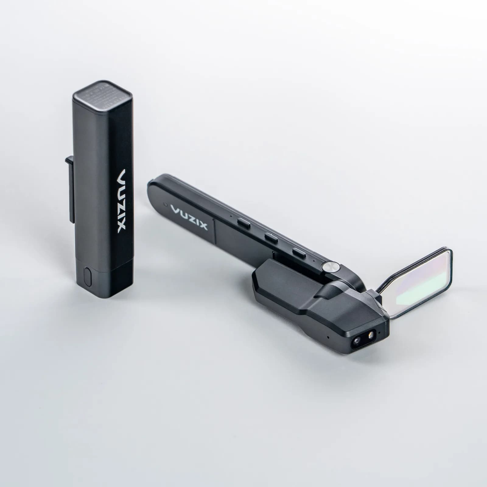 El módulo del Vuzix M4000 sobre una superficie blanca junto a su batería negra en forma de barra, con la guía de onda transparente reflejando color al frente.