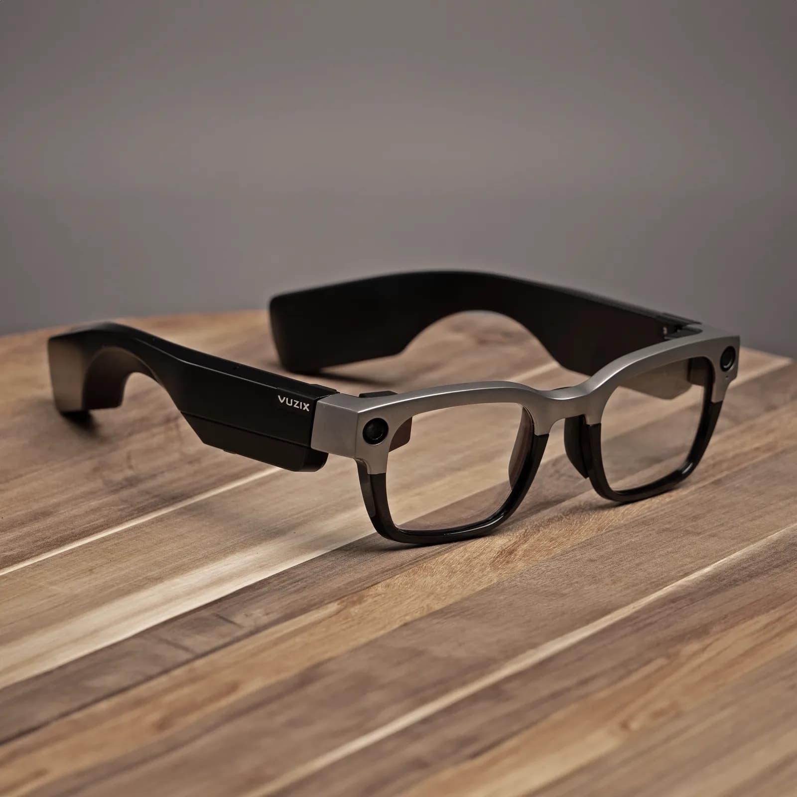 Vuzix Shield glasses folded on a wood table, thick black frame with a titanium brow bar and a camera on the temple.