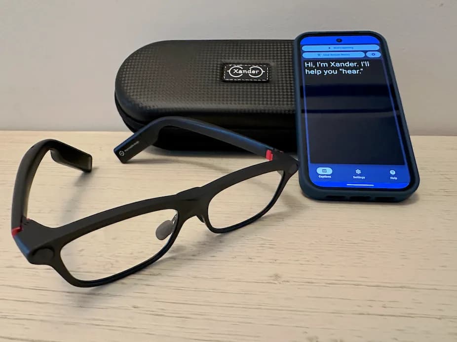 XanderGlasses in black with a thick rectangular frame and red hinge accents, on a table beside their case and a phone.