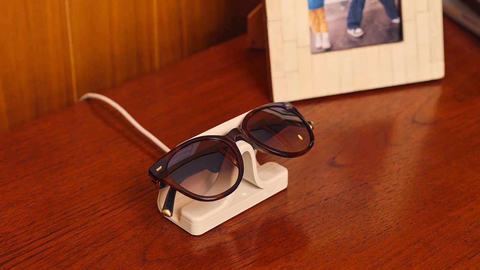 Amazon Echo Frames in tortoiseshell brown, round shape, resting on a white charging stand with a small green light indicator.