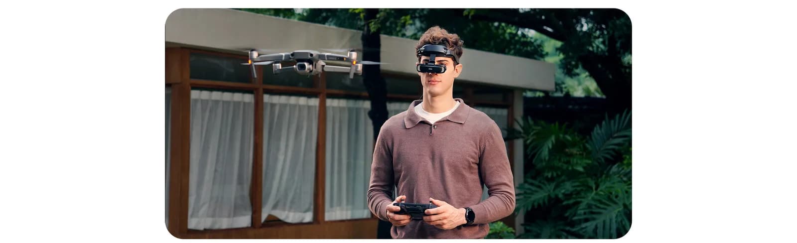 GOOVIS Art worn by a man outdoors while he holds a remote control, with a drone flying near a house behind him.