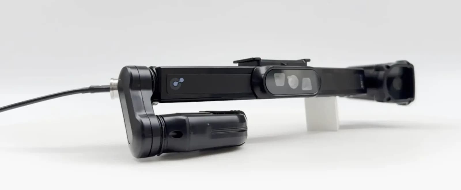 Iristick H1 head-mounted module in black, an articulated arm with a camera and display unit on one end and a cable on the other, gray background.