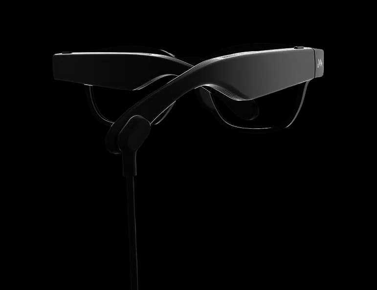 Mentra Live glasses in black with a charging cable attached, hanging below the folded frame.