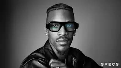 Un hombre usa gafas Snap Specs negras de montura rectangular gruesa, en primer plano, con un tono verdoso visible en los cristales.