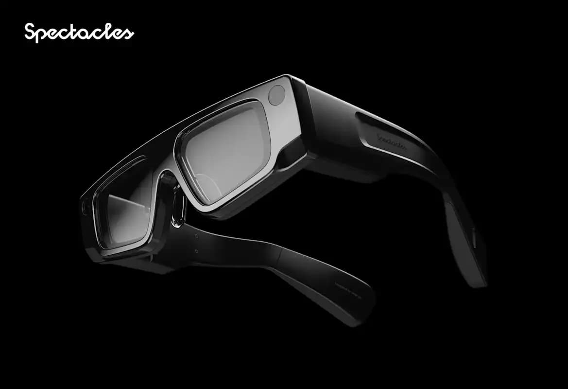 Snap Spectacles 5th Generation AR glasses in black with a bulky wraparound frame, shown at an angle with a camera lens on the front corner.