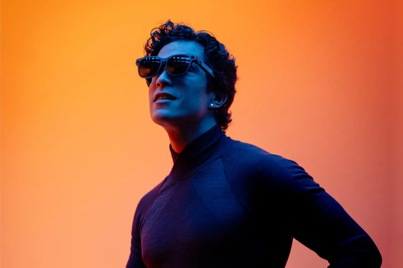 A man wears black VITURE Luma Ultra glasses, seen from the front in a portrait lit against an orange background.