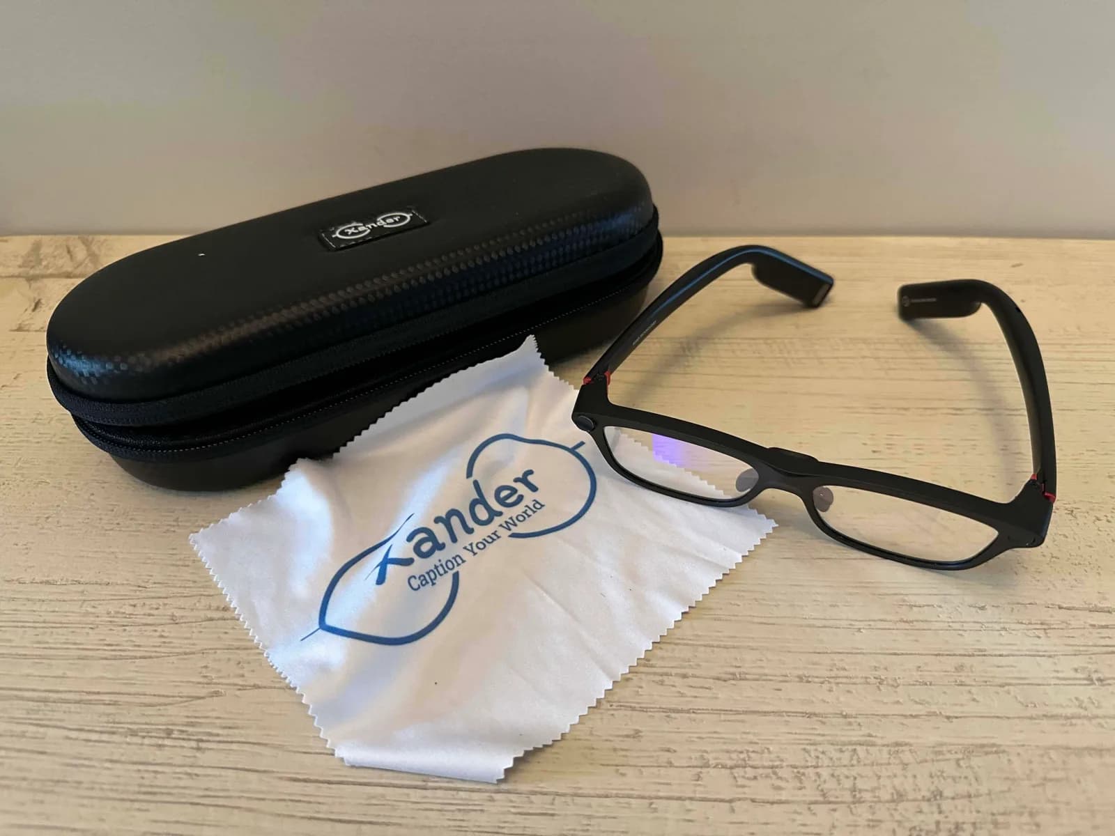 XanderGlasses folded on a table next to their hard case and a cleaning cloth printed with the Xander logo.