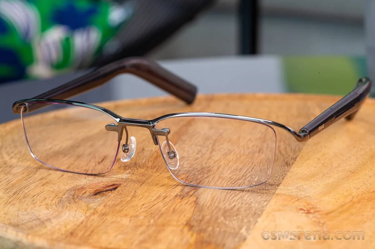 Xiaomi MIJIA Smart Audio Glasses in a thin rimless metal frame, resting on a wood table, with 'mijia' on the temple tip.