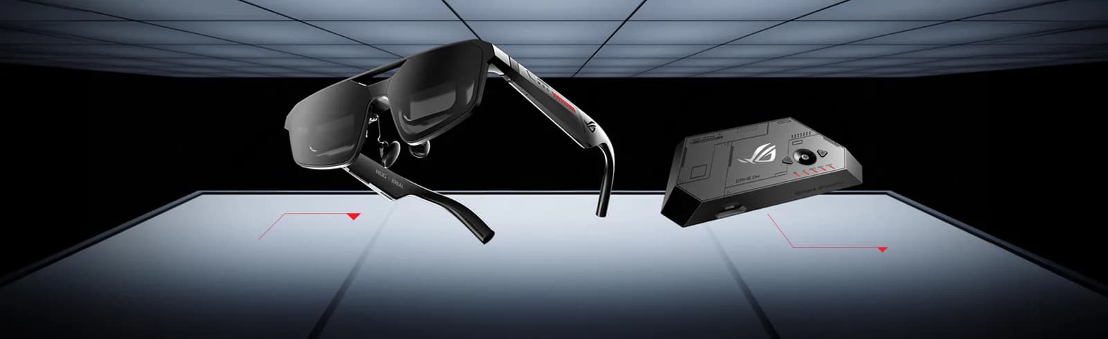 ROG XREAL R1 glasses in gunmetal, with red ROG branding on the temple, resting on a glass surface next to a small gray control box.